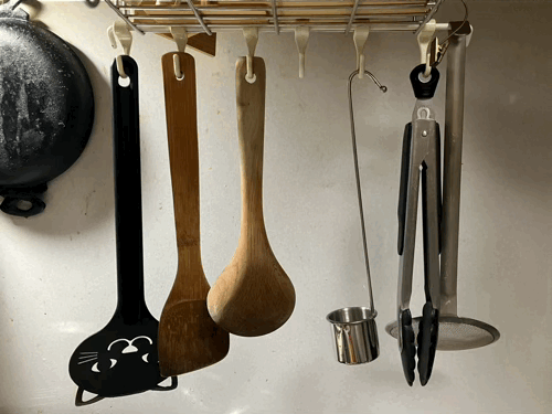 GIF 台所のキッチン道具掛けにフライ返し、木べら、木のおたま、レードル、トング、かす揚げがかかっている。GIFの2枚目ではレードルに本を読むノラネコ軍団のネコが1匹入って本を読んでいる。これではシードルが使えないではないか!実用的だったのに非実用的なものになってしまった!